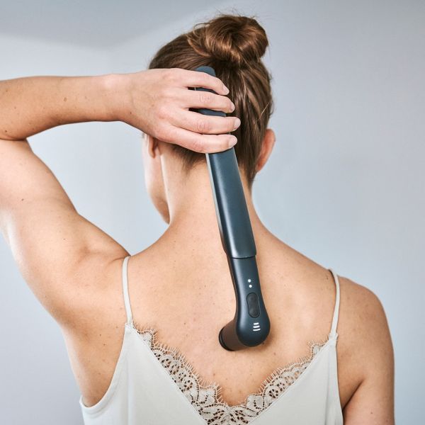 Frau verwendet ein Novafon Schallwellengerät zur Rücken- und Nackenmassage.