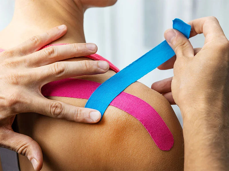 Kinesiotape Anlagen in Blau und Pink auf der rechten Schulter einer Frau