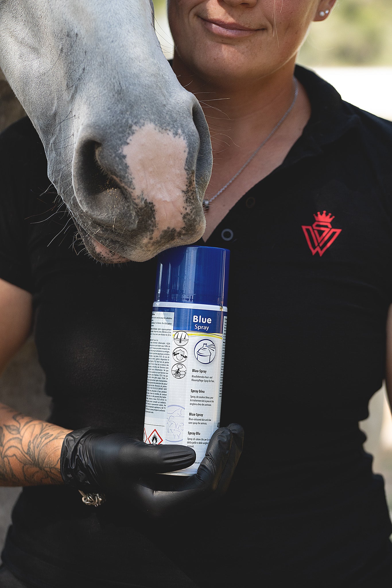 Mitarbeiterin hält eine Dose Kerbl Blue Spray in der Hand, ein Pferd schaut über ihre Schulter im Stall