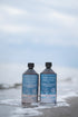Totes Meer Salzsole 2,5% & 5% 1 Liter Flaschen im Set am Strand im Meerwasser stehend