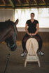 Reiterin trainiert auf dem HORSE bodyforming Balance Rider in der Reithalle, während ein Pferd im Vordergrund zuschaut